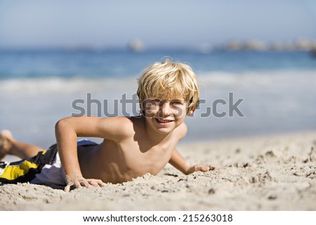 Blonde boy lying on sandy beach, smiling, portrait