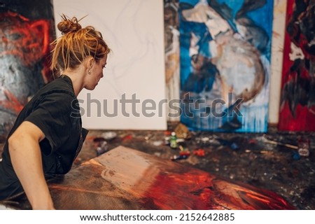 Gorgeous female painter artist creating in a spacious workshop. Painting an art piece on a large canvas with a paint brush. Creative young woman making a painting for her new art project.