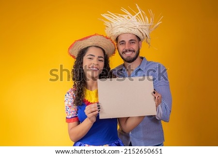 Brazilian couple wearing traditional clothes for Festa Junina holding a sign with copy space