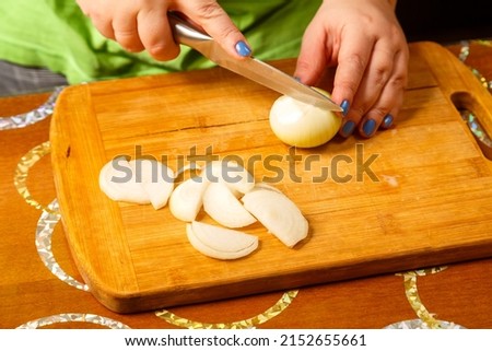 Women's hands cut onions with a knife on a wooden board. Horizontal photo