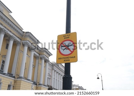 A yellow warning sign restricting the flight of quadrocopters and drones hangs on a pole. It says: no-fly zone