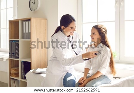 Happy child smiling while doctor is examining her lungs or heart during medical checkup in sunny office. Cheerful pediatrician using stethoscope to check respiration and heartbeat of her young patient Royalty-Free Stock Photo #2152662591