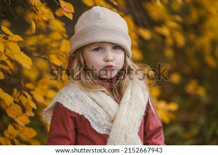 Little girl blow your lips on the background of yellow foliage