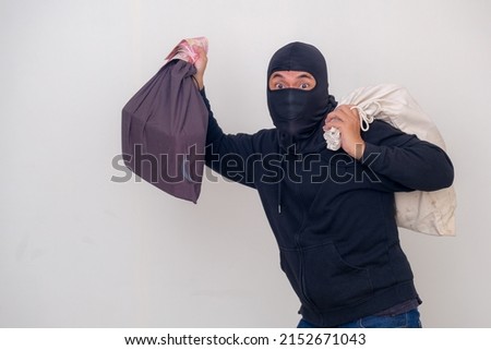 A man wearing a black balaclava and black hoodie carrying money and two sacks of   goods  Royalty-Free Stock Photo #2152671043