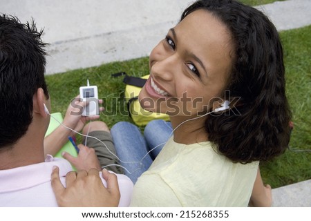 Teenage couple listening to MP3 player, sharing headphones, smiling, portrait, elevated view