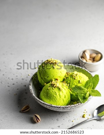 Tasty pistachio ice cream with mint garnished with crushed pistachios on textured background, closeup view