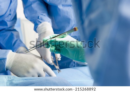 Surgeons in scrubs and surgical gloves operating on patient, focus on tweezers, close-up