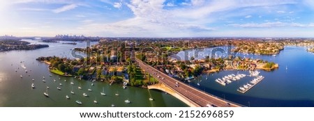 Aerial panorama over Gladesville bridge across Parramatta river in Sydney West facing distant city CBD skyline.
