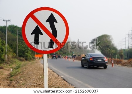 Traffic road sign with symbols of arrows to warn drivers do not overtake that can cause car accidents beside the rural road.                                        