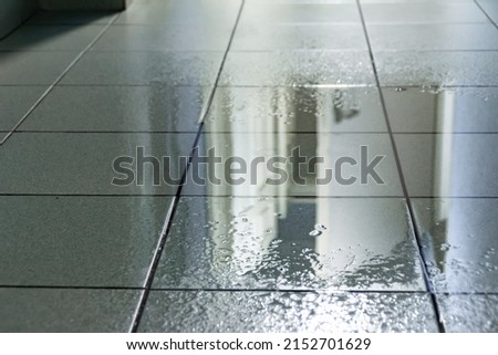 a large puddle on the tiled floor was caused by water from the ceiling as a result of a roof leak or a burst water pipe, selective focus Royalty-Free Stock Photo #2152701629