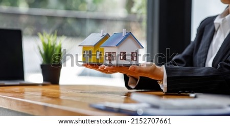 Businessmen and customers are signing home purchase agreements. Hand holding the pen signing purchase contract. Gray roof houses and keys placed close to each other.Real estate mortgage home purchase.