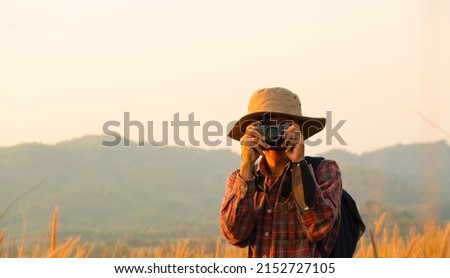 Asian man holding a camera with both hands.man wearing a hat taking pictures,copy space.