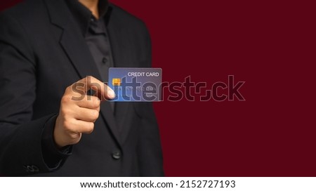 Businessman in a suit holding a mockup blue credit card while standing on a red background in the studio. Close-up photo. Business and finance concept