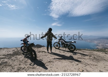 Female motorcyclist relaxing in dirt motorcycle travel on mountain cliff, beautiful sea shore and mountains landscape on background 