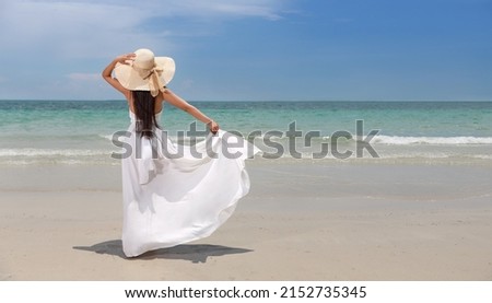 Back view young happiness asian traveller woman in white dress and hat standing on beautiful sandy beach. Cute girl enjoy her tropical sea on relax holiday vacation during summer time and sunshine day Royalty-Free Stock Photo #2152735345
