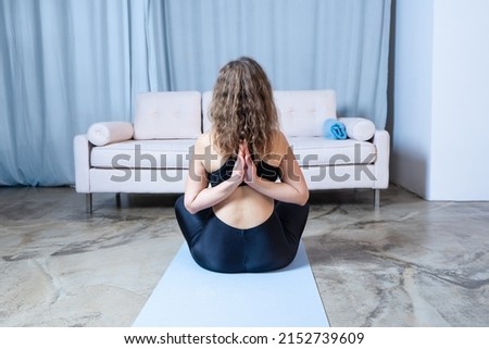Young healthy beautiful woman in sports top and leggings practicing yoga at home, sitting in pose on yoga mat. namaskarasana