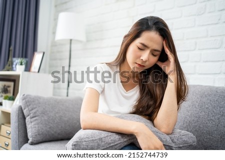 Beautiful Asian woman wearing white T-shirt feeling stress and headache on sofa. She used her hand to touch her face. Office syndrome concept. Royalty-Free Stock Photo #2152744739