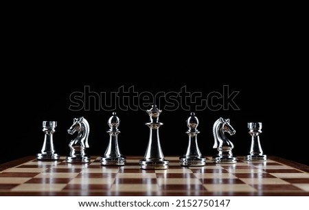 Shiny steel chess figures standing on wooden chessboard. Intellectual duel and tactical battle symbol. Strategy planning and corporate leadership concept. Silver metal chess pieces on black background Royalty-Free Stock Photo #2152750147