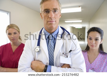 Mature male doctor flanked by two female nurses, standing in hospital corridor, portrait