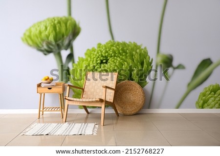 Wooden armchair and table near light wall with printed flowers