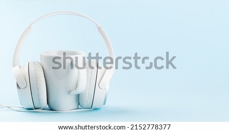 White headphones and cup of coffee over blue background with copy space. Podcast, audiobook or music template
