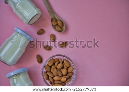 Almonds and almond drink in glass jars on pastel pink background. Healthy lifestyle and diet concept. Top view. space for text.
