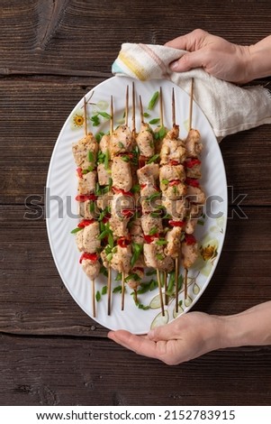 Grilled vegetable and chicken skewers with bell peppers, zucchini, onion and mushrooms on a wooden table in female hands, top view. Meat and vegetables kebabs on skewers.