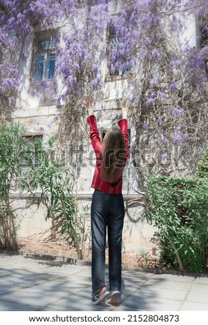 Pretty young woman is standing next to wisteria. Girl enjoying spring time. Spring outfit.