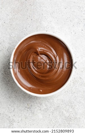 Chocolate sauce, cream in a white saucer on grey background. Curl of Liquid chocolate. Top view.