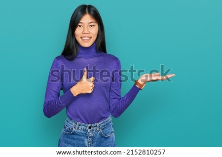 Beautiful young asian woman wearing casual clothes showing palm hand and doing ok gesture with thumbs up, smiling happy and cheerful 