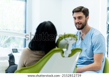 Male dentist in dental office talking with female patient and preparing her for treatment. Explaining the procedure of new dental implants.Rear view of the patient, focus on a dentist. Royalty-Free Stock Photo #2152812739