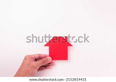 top view of  holding cutout red paper plain house by fingers on white paper background in concept of business banking and outstanding.