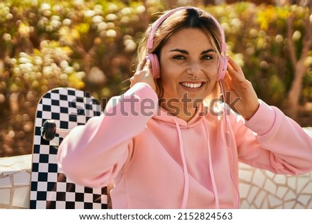 Young blonde skater girl smiling happy using headphones sitting at the park