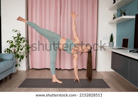 Young  woman doing half moon pose at home. Athletic female balancing on one leg in yoga position. Active lifestyle, pilates, fitness exercise, taking care of body concept. 