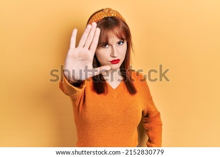 Redhead young woman wearing casual orange sweater doing stop sing with palm of the hand. warning expression with negative and serious gesture on the face. 