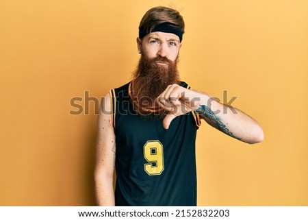 Redhead man with long beard wearing basketball uniform looking unhappy and angry showing rejection and negative with thumbs down gesture. bad expression. 