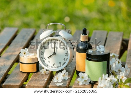 Vintage alarm clock and cosmetic bottle and jar on wooden table spring time garden 