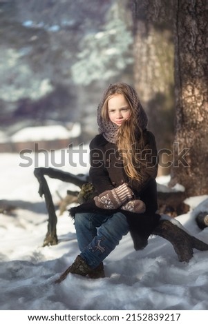 cute caucasian girl wearing warm coat, wool mittens and shawl holding bunch of tulips on cold winter day. Image with selective focus