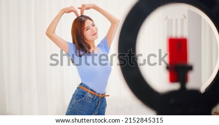 asian brunette shoulder length hair female social media influencer is doing streaming and dancing to audience with phone - she poses big heart shape 