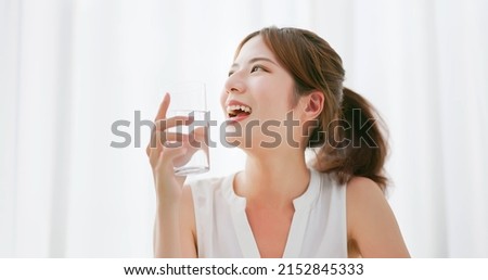 close up of asian woman with brunette ponytail smile drinks a glass of water happily in a white room Royalty-Free Stock Photo #2152845333