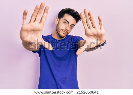 Young hispanic man wearing casual t shirt doing frame using hands palms and fingers, camera perspective 