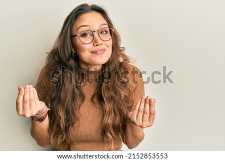 Young hispanic girl wearing casual clothes and glasses doing money gesture with hands, asking for salary payment, millionaire business  Royalty-Free Stock Photo #2152853553
