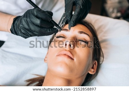 Cosmetologist measures the proportions of the eyebrows with the ruler. Micropigmentation work flow in a beauty salon. Royalty-Free Stock Photo #2152858897