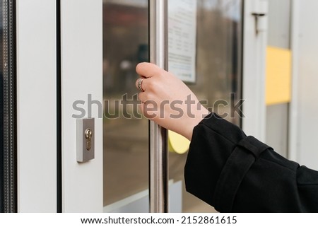 Woman opening office door outside, side view. Close-up of woman's hand holding chrome glass door handle outdoors.