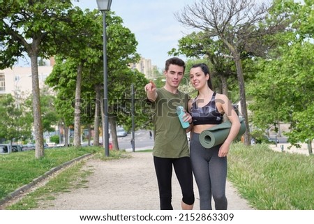 Young sport couple pointing and looking at something or somewhere while standing at a park. Fitness concept.