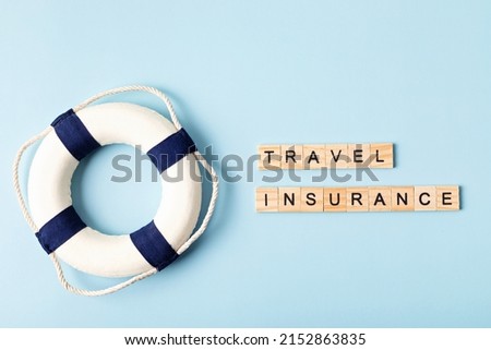 Safe travel, protection tourism insurance concept. Travel insurance wooden letters and lifebuoy over blue background. Top view, flat lay.