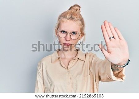 Beautiful caucasian woman with blond hair wearing casual look and glasses doing stop sing with palm of the hand. warning expression with negative and serious gesture on the face. 