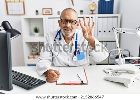 Mature doctor man at the clinic showing and pointing up with fingers number four while smiling confident and happy. 
