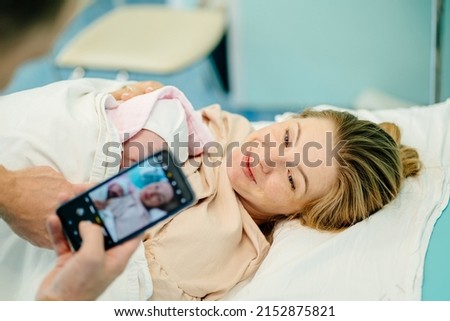 Family in the delivery ward. Supportive father making firstb photo of his baby and wife.