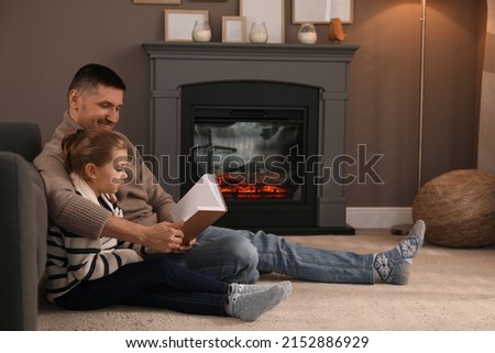 Happy father and daughter reading book together on floor near fireplace at home Royalty-Free Stock Photo #2152886929